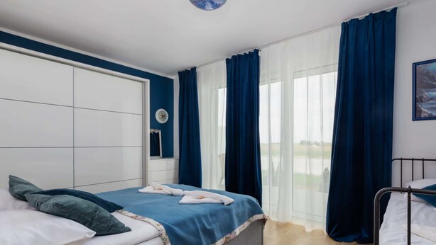 Un dormitorio con cama, mesita de noche, ventana con cortinas y vistas al exterior.