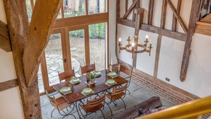 Un comedor con una mesa de madera dispuesta para seis personas, rodeada de sillas, y vistas al jardín a través de grandes ventanales.