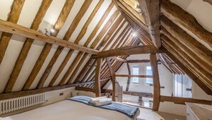 Un dormitorio con techo inclinado, vigas de madera, una cama, un radiador y una ventana.