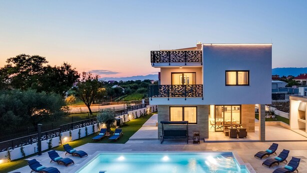 A modern two-story house with a swimming pool, lounge chairs, and a well-lit outdoor area. - Villa Kate ZadarVillas (Poljica-Brig)