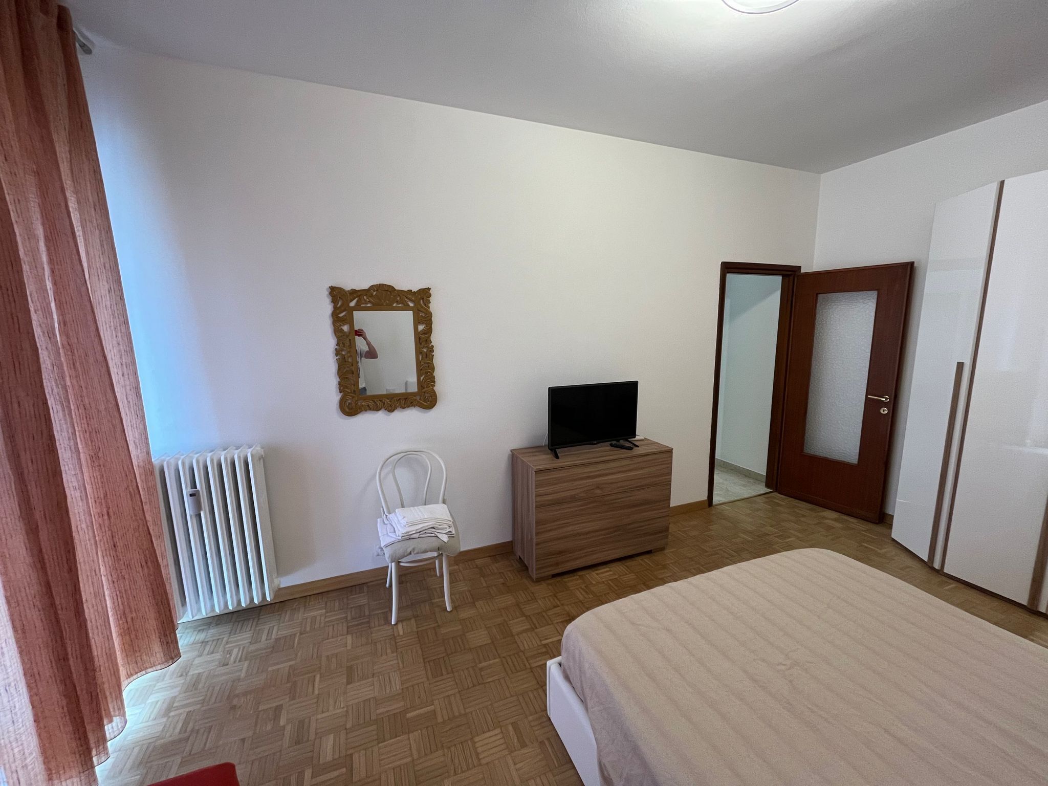A bedroom with a bed, a dresser, a television, a mirror, and a wardrobe.
