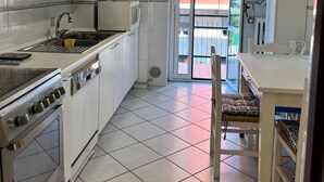 Cuina compacta amb armaris blancs, fogó i zona de menjador amb una cadira.