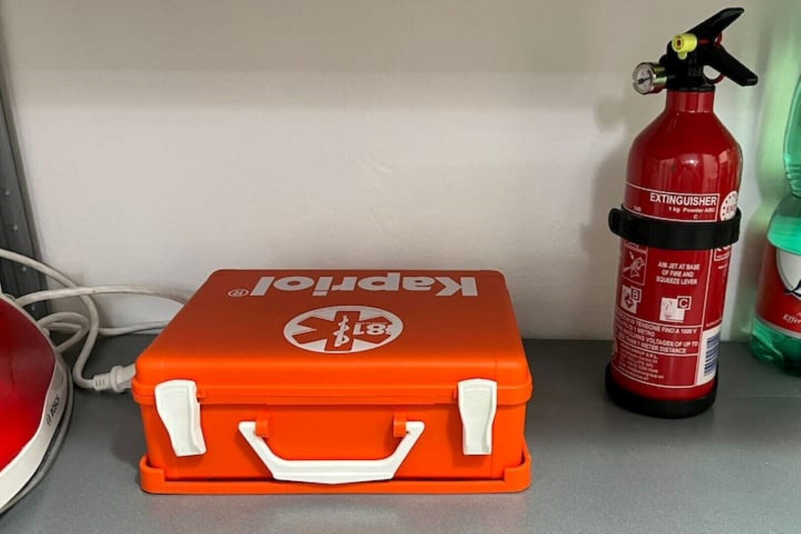 Punainen palosammutin, vihreä pullo ja oranssi työkalulaatikko, jossa on valkoinen kahva.