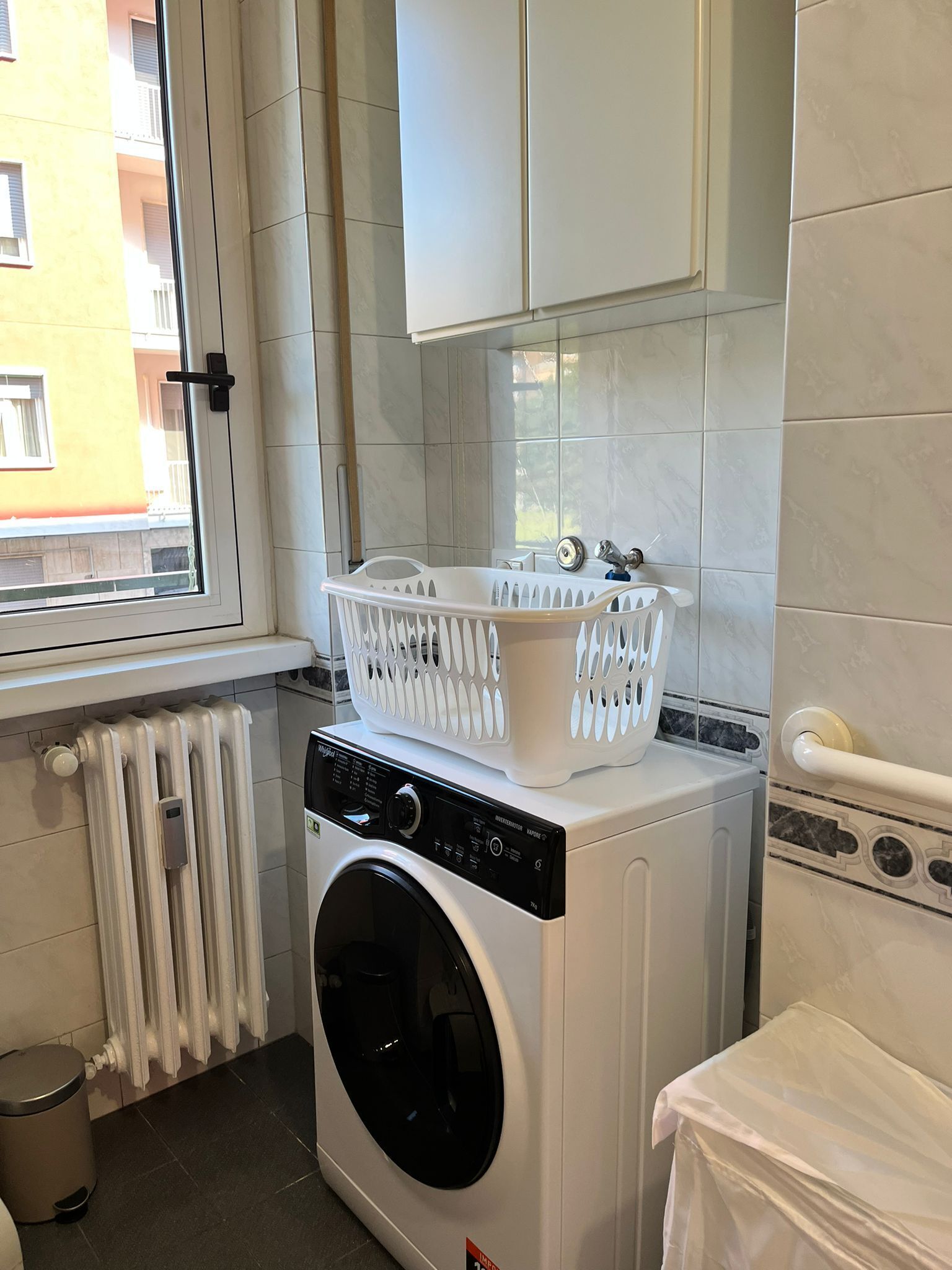 A compact laundry room with a front-loading washing machine, a drying rack, and a radiator.