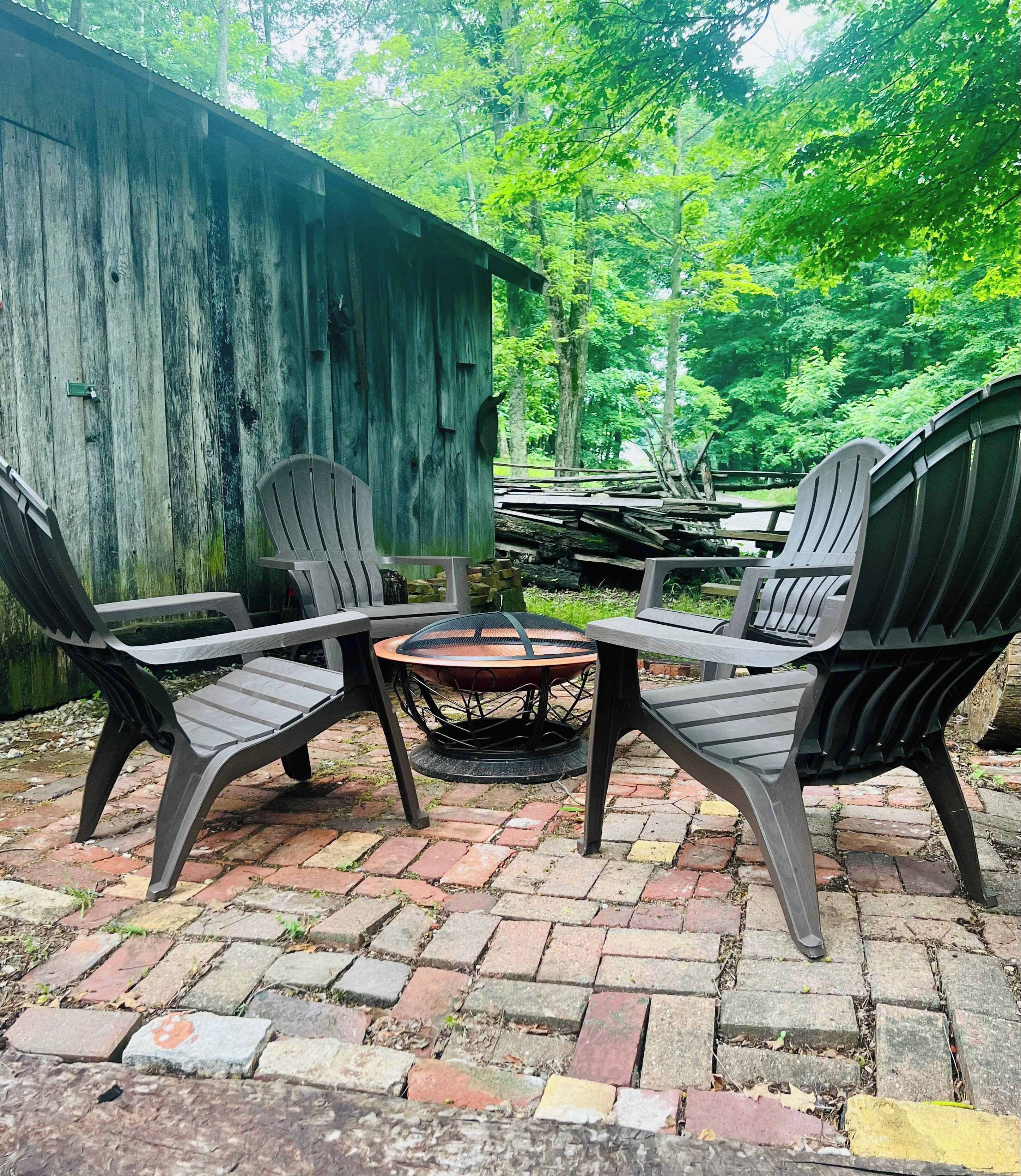 A patio with four Adirondack chairs and a round table, surrounded by a wooden fence and lush greenery.