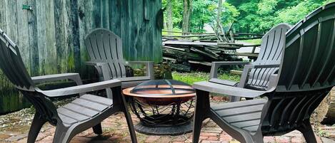 A patio with four Adirondack chairs and a round table, surrounded by a wooden fence and lush greenery.