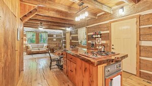 L’intérieur d’un chalet rustique, avec un revêtement mural en bois, un coin cuisine doté d’un grand îlot central et un espace salon confortable avec un canapé et des fauteuils.