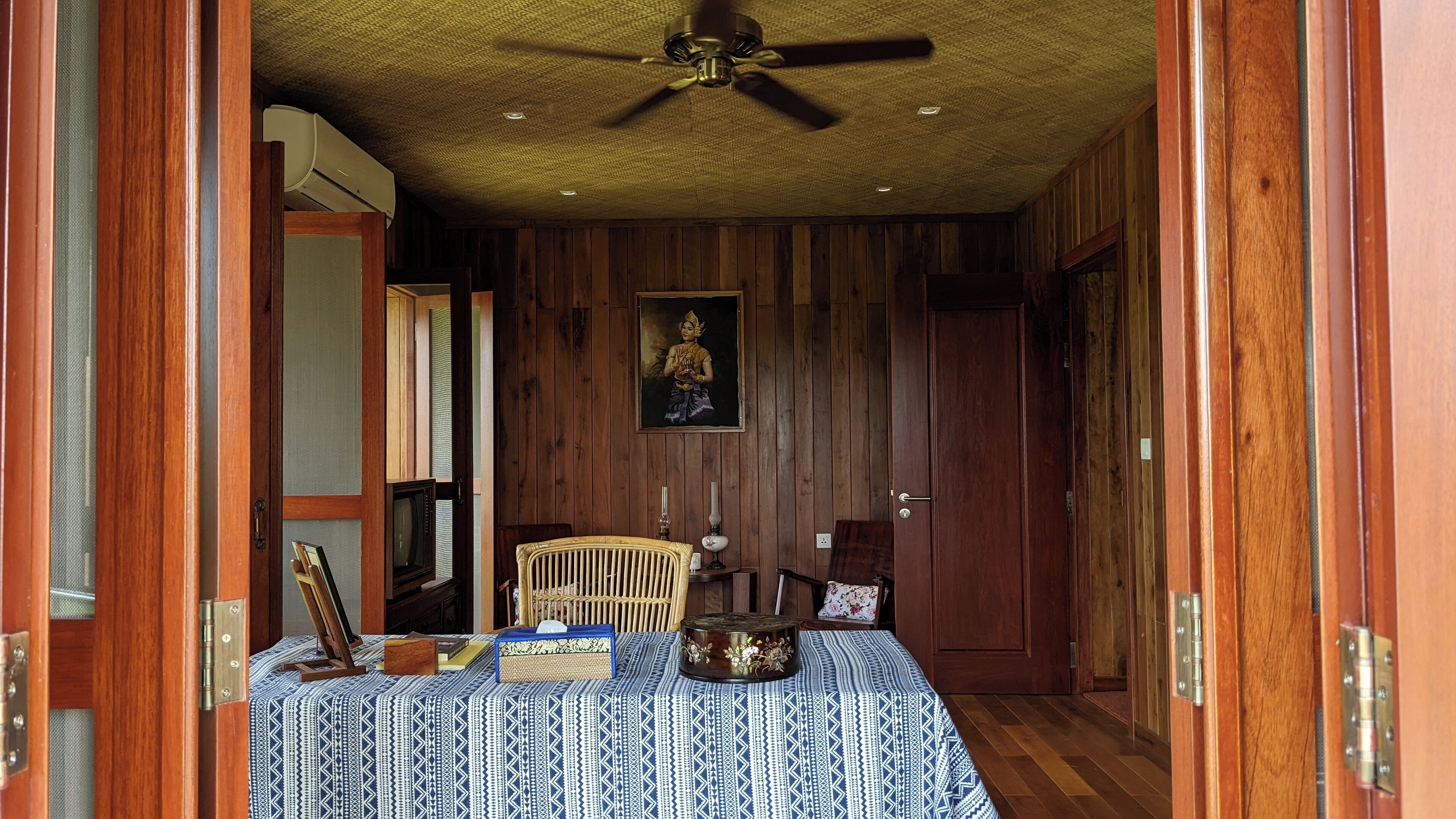 A room with a bed, a ceiling fan, a painting, and wooden walls.