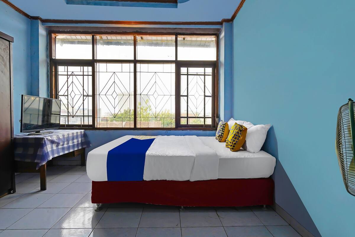 A bedroom with a bed, a TV, a table with a checkered tablecloth, and a window with metal bars.