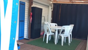 Ein überdachter Patio-Bereich mit Holzterrasse, Tisch und Stühlen sowie einer blauen Tür.