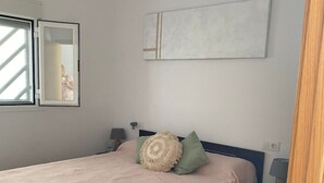 A bedroom with a bed, a nightstand, a lamp, and a wall-mounted artwork. - Chalet con Piscina Privada (Chiclana de la Frontera)