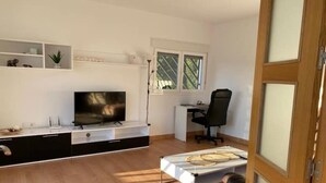 A modern living room with a flat-screen TV, a desk, and a black office chair. - Chalet con Piscina Privada (Chiclana de la Frontera)