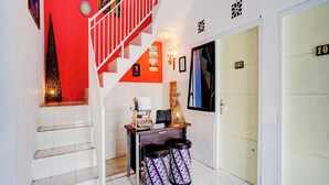 Uma escadaria com parede vermelha e grades brancas, um balcão de recepção com uma placa e uma porta com a inscrição "102".