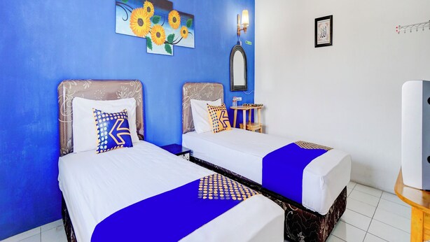 Quarto de hotel com duas camas, parede azul, pintura de girassóis, espelho e uma pequena mesa com abajur.