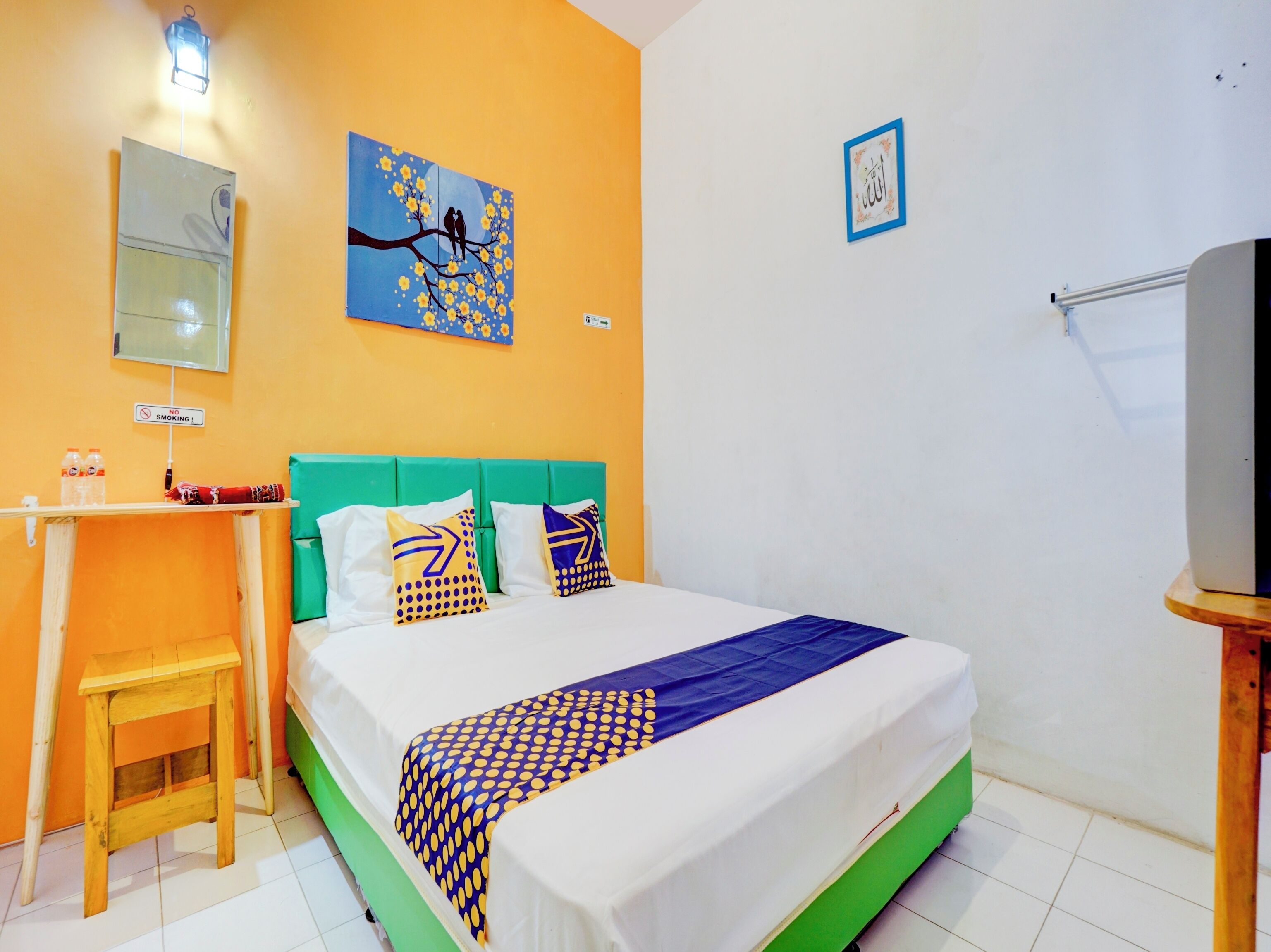 Quarto de hotel com cama, escrivaninha, cadeira, televisão e um quadro na parede.