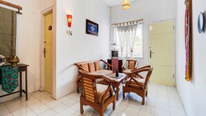 Uma área de refeições com cadeiras de madeira e uma mesa, uma televisão em um suporte, um pendurar de parede estampado e uma porta com cortina.