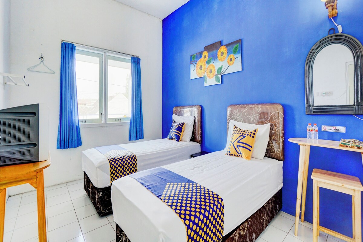 A hotel room with two beds, a TV, a mirror, and a blue wall with sunflower artwork.