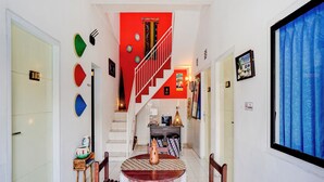 Um corredor com escadaria que leva a um quarto, área de jantar com mesa e cadeiras, e cortina azul à direita.