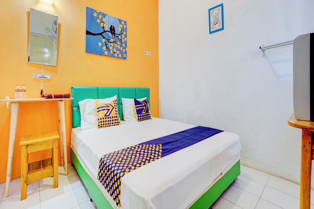A hotel room with a bed, a desk, a chair, a TV, and a painting on the wall.