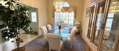 A dining area with a glass table, cushioned chairs, a chandelier, and a cabinet with glass doors.