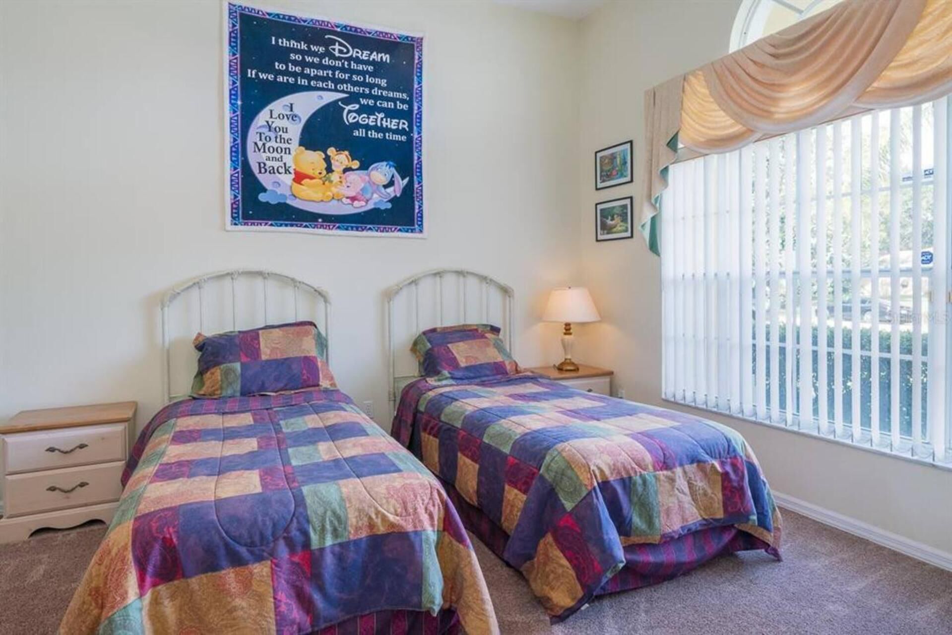Een slaapkamer met twee bedden, een nachtkastje met lamp, een raam met zonwering en een poster aan de muur.
