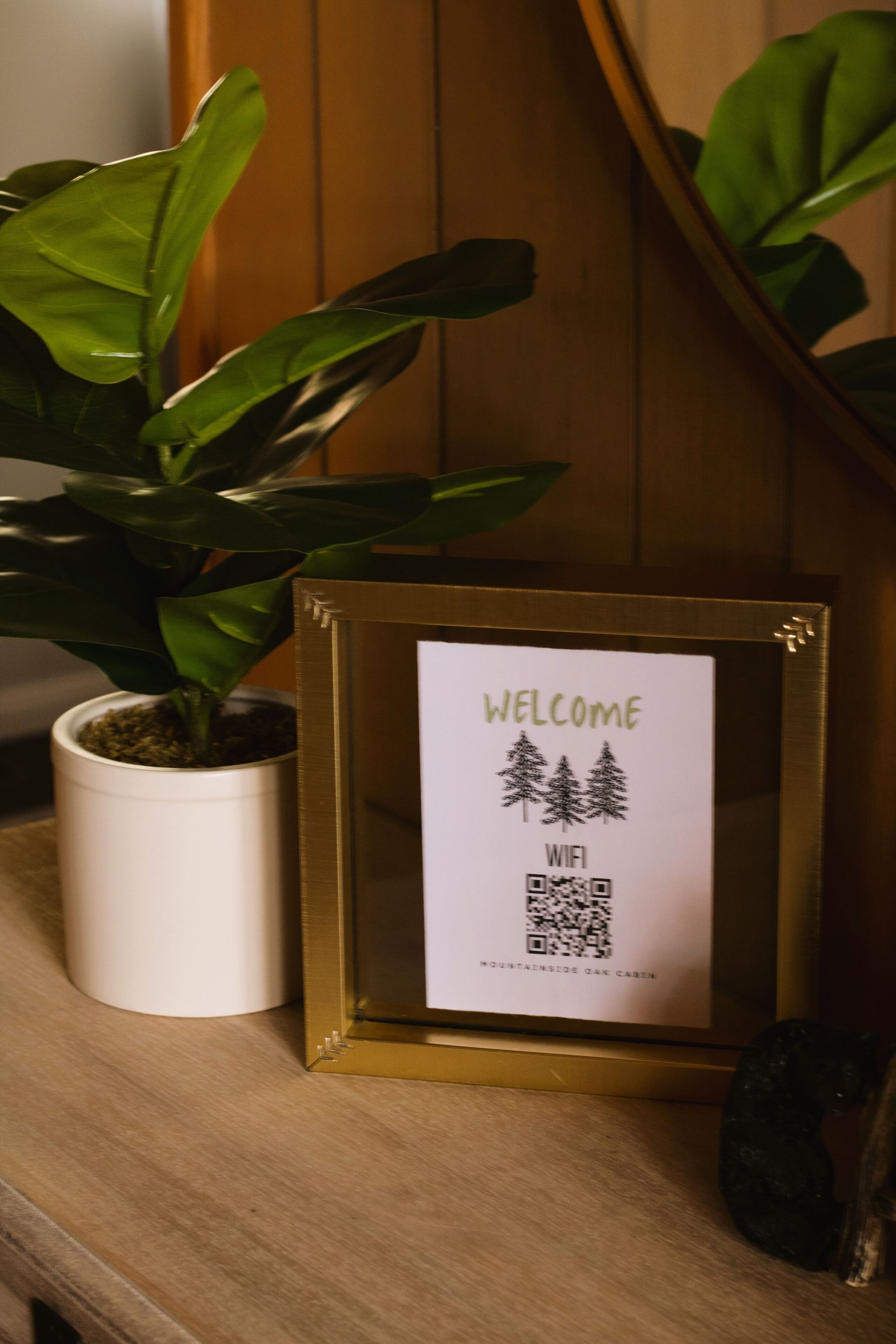 A framed welcome sign with a QR code and a potted plant beside it.
