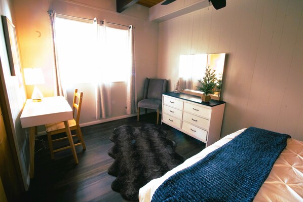 Un dormitorio con cama, escritorio, silla, cómoda y un ventanal grande.