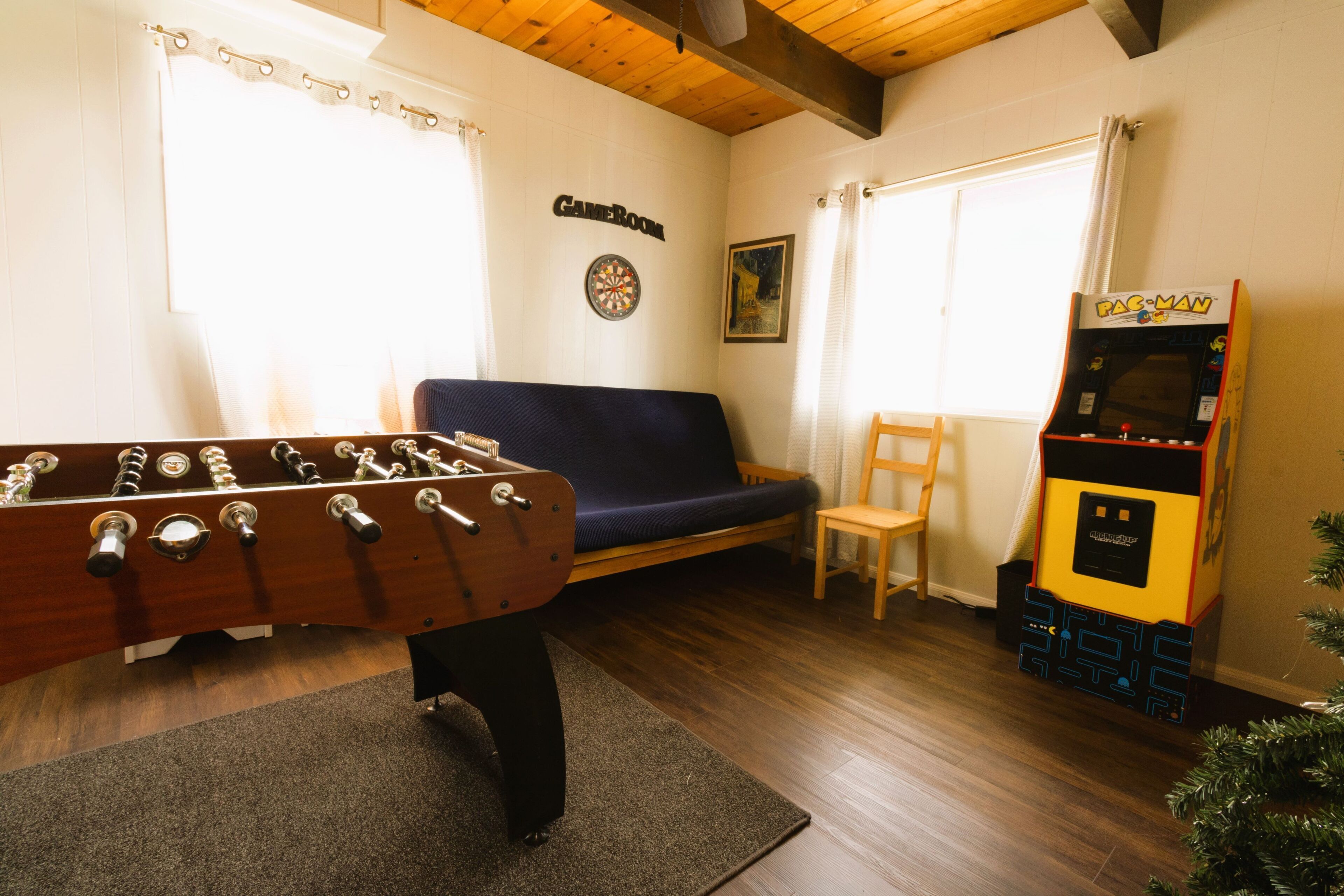 A room with a foosball table, a sofa, a dartboard, and a Pac-Man arcade machine.