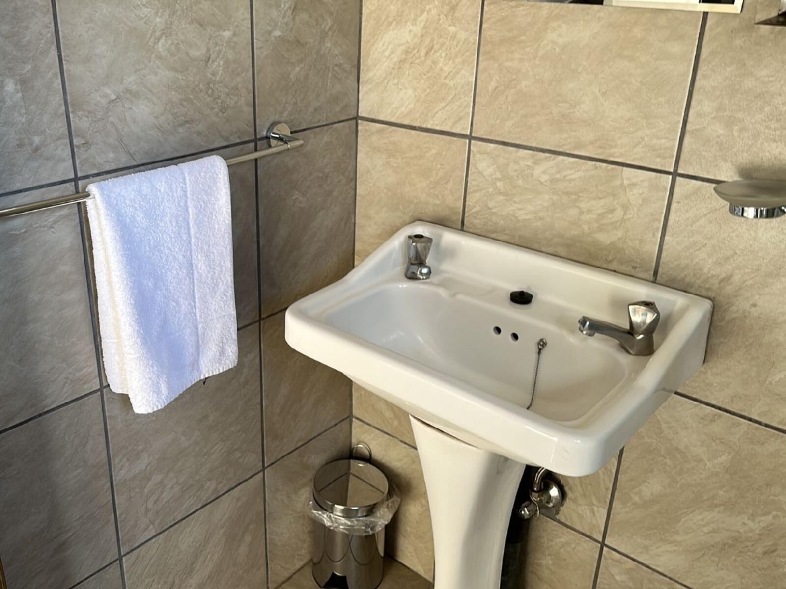 A bathroom with a white sink, a towel hanging on a rack, and a trash can.