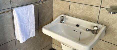 A bathroom with a white sink, a towel hanging on a rack, and a trash can.
