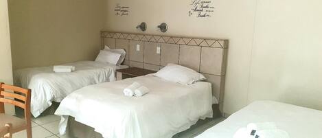 A hotel room with two beds, a wooden chair, and a wall with decorative text.