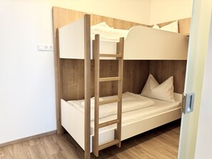 Ein Etagenbett mit Holzleiter, weißer Bettwäsche und einem Holzkopfstück.