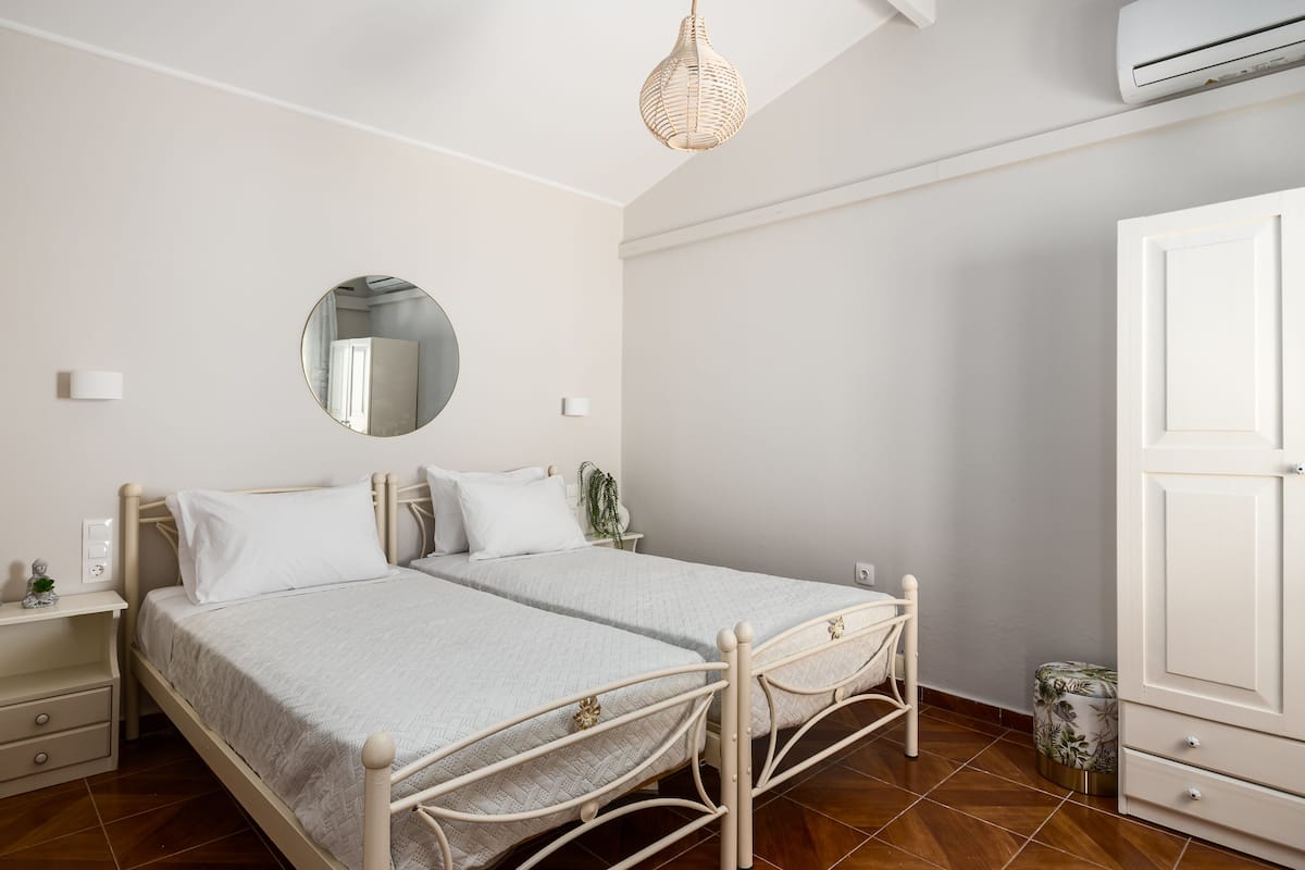 A bedroom with two beds, a round mirror, a hanging light fixture, and a wardrobe.