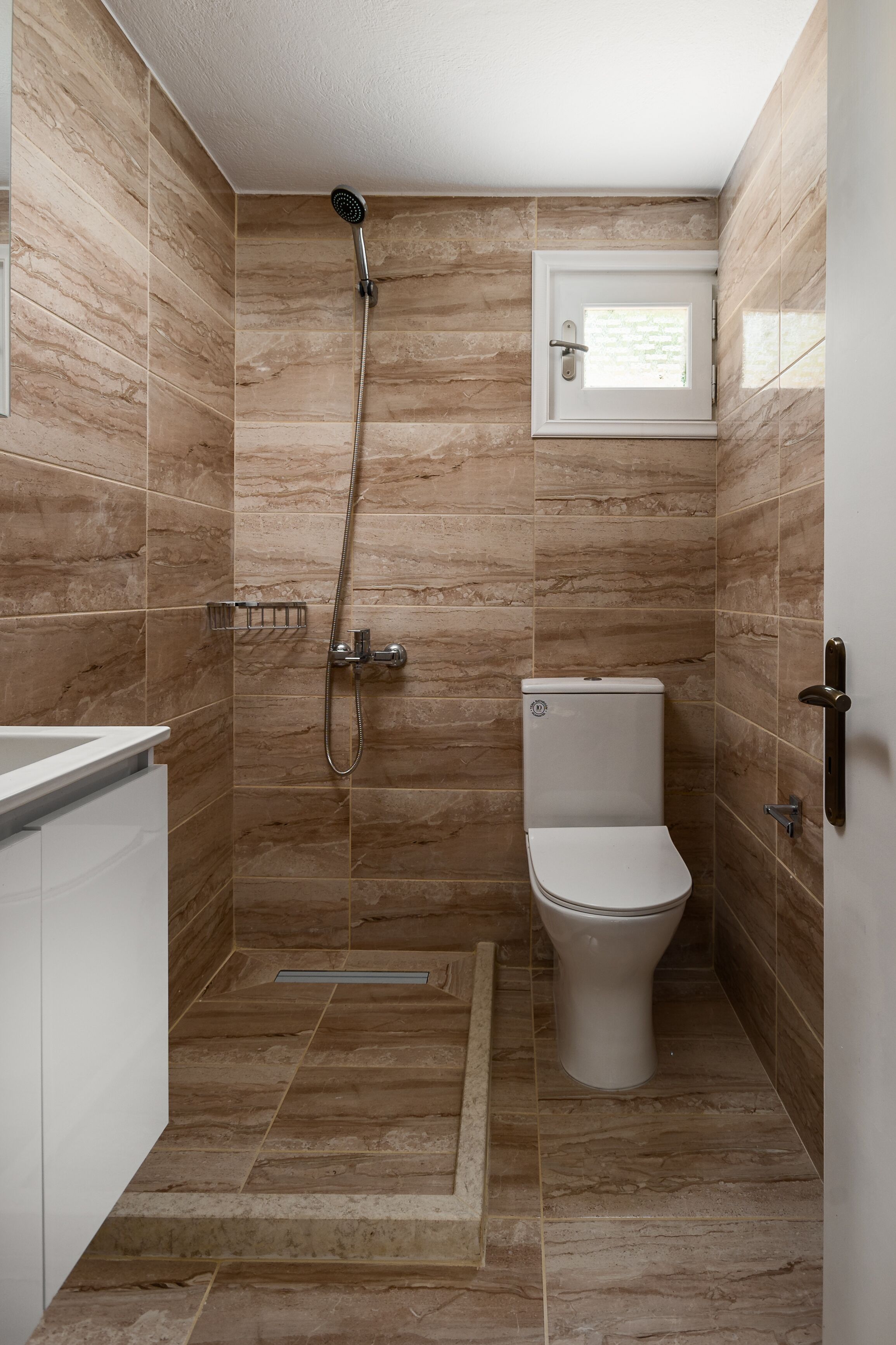 A small bathroom with a shower, toilet, and a window.