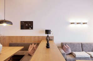 Ein modernes Interieur mit einem Holztisch, einem grauen Sofa und einer schwarzen Vase, darüber eine Wandleuchte.