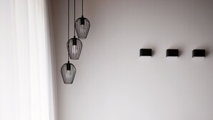 Un saló modern amb un sofà gris, una taula de centre i una cadira. Hi ha tres llums penjants del sostre i tres llums fixats a la paret.