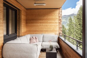 A wooden balcony with a sofa and a small table, overlooking a mountainous landscape. - Alpenstolz #1.03 Comfort (Damüls)