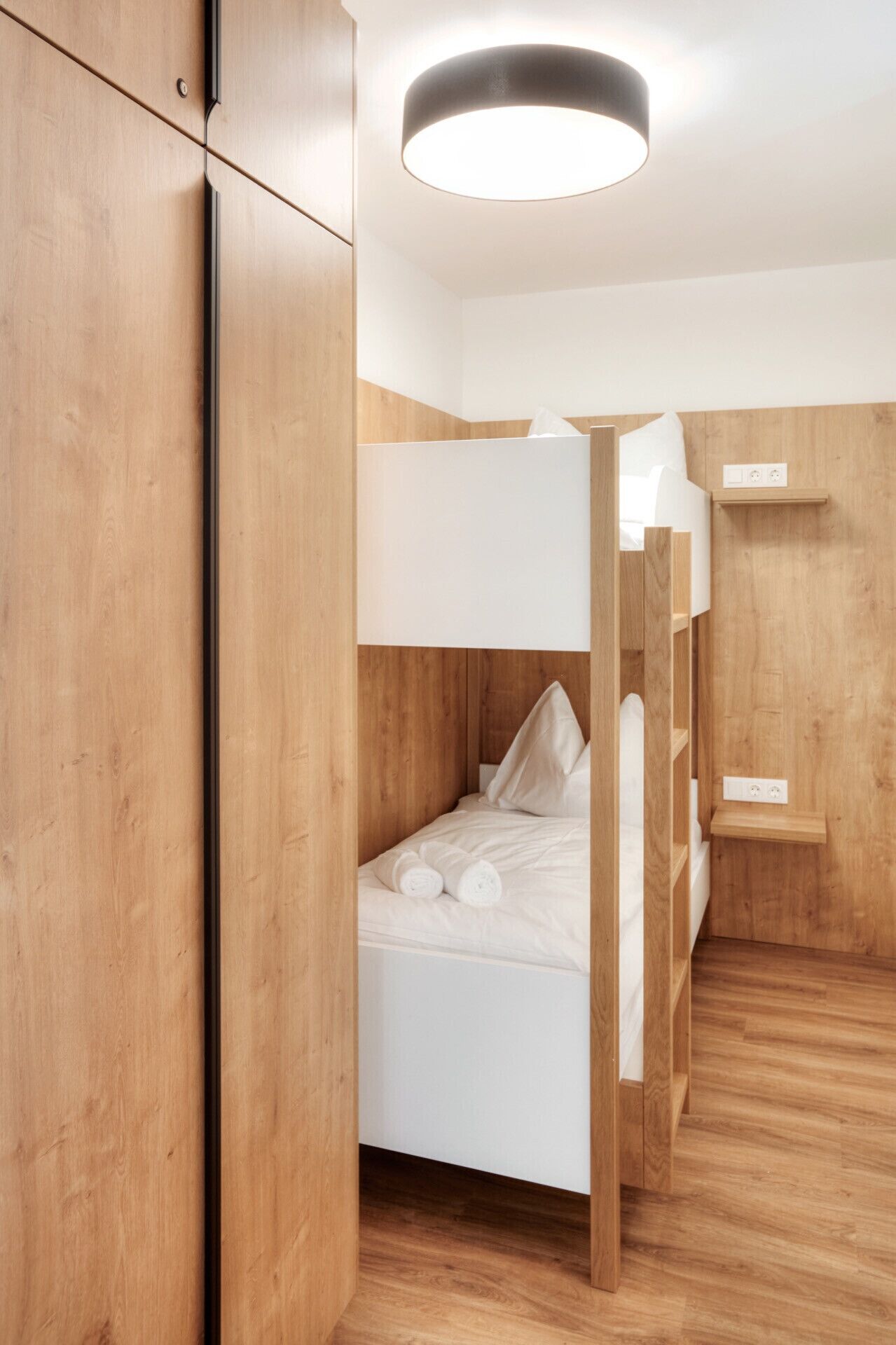 A modern, minimalist bedroom with a bunk bed, wooden walls, and a ceiling light.