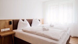 A hotel room with a wooden headboard, white bedding, and a bedside table with a power outlet. - Alpenstolz #1.07 Comfort (Damüls)