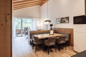 A modern kitchen with a wooden dining table, chairs, and a built-in microwave. - Alpenstolz #1.09 Exclusive (Damüls)