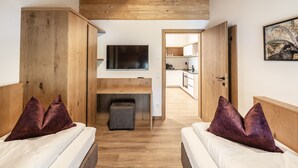 Ein modernes Schlafzimmer mit Holzbalken, einem Flachbildfernseher, einer kleinen Sitzecke und einer Küche im Hintergrund.