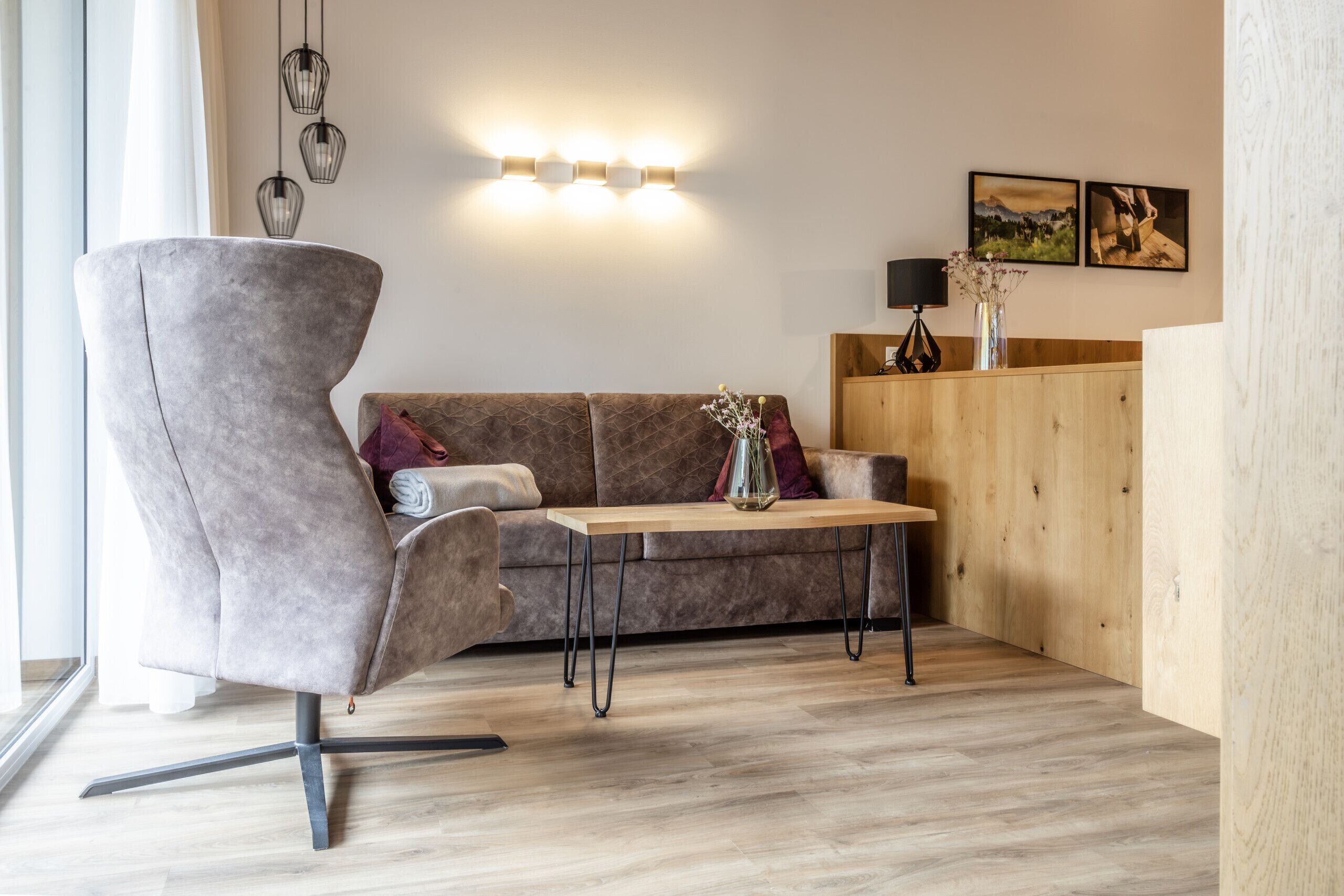Ein modernes Wohnzimmer mit einem grauen Sessel, einem braunen Sofa, einem Holztisch und einer Wandleuchte.