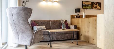 Ein modernes Wohnzimmer mit einem grauen Sessel, einem braunen Sofa, einem Holztisch und einer Wandleuchte.
