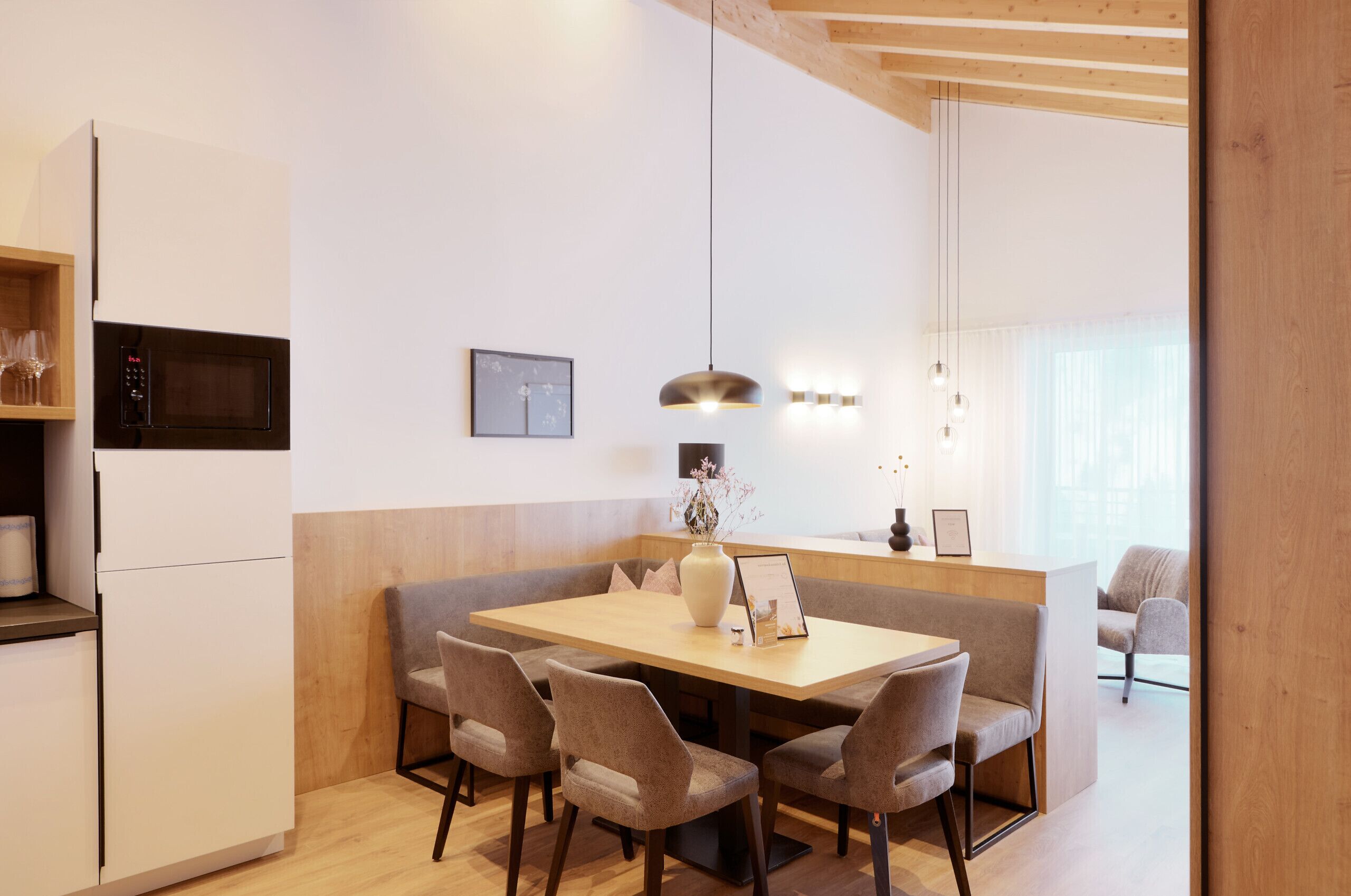 A modern kitchen with a built-in microwave, a wooden dining table with chairs, and a pendant light.