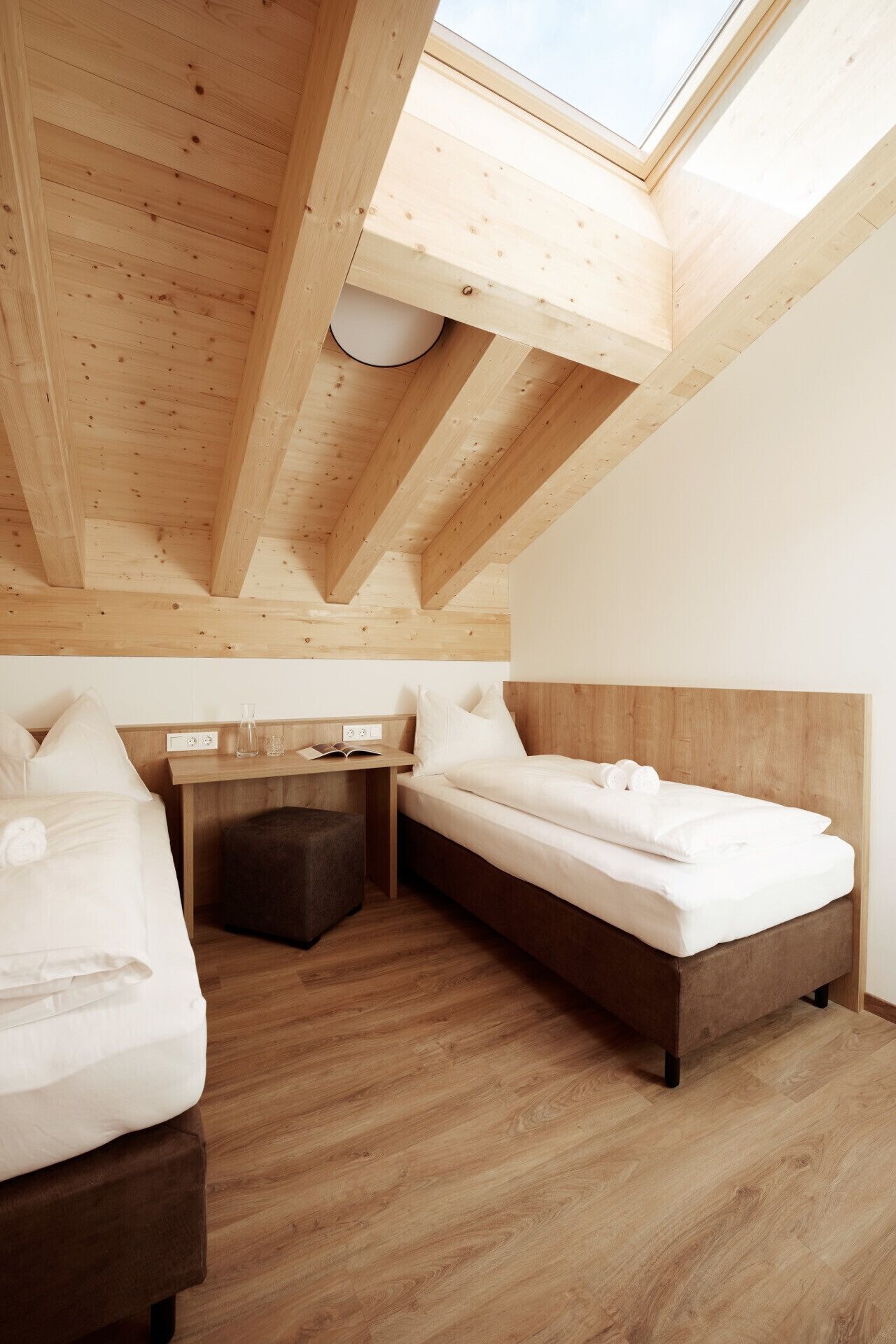 Une chambre avec une lucarne, des poutres apparentes, un bureau et deux lits.
