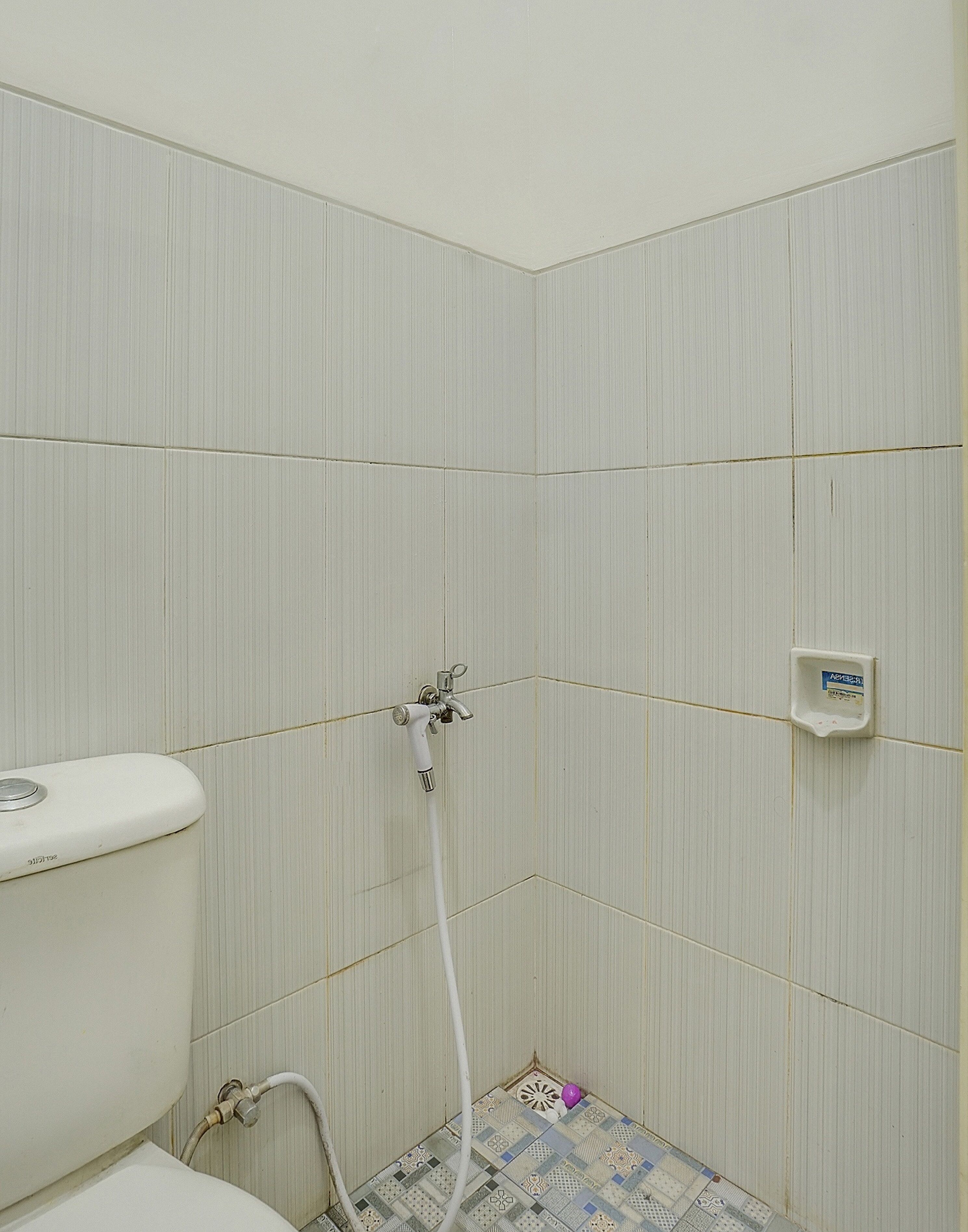 Ein Badezimmer mit Toilette, einer Dusche inklusive Duschschlauch und Fliesenboden.
