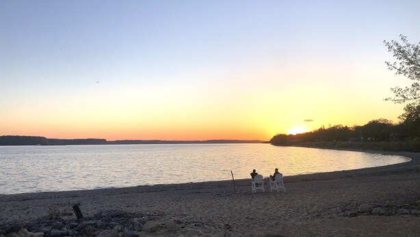 En strand med två vita stolar som är placerade så att de vetter mot solnedgången över ett stilla hav.
