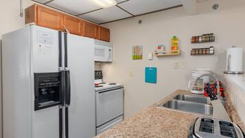 Une cuisine équipée d’un réfrigérateur, d’un four à micro-ondes, d’une cuisinière et d’un évier. On y trouve des placards, un plan de travail et divers ustensiles de cuisine.