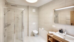 A modern bathroom with a glass shower enclosure, a toilet, and a sink with a mirror. - Alpenstolz #1.06 Comfort (Damüls)