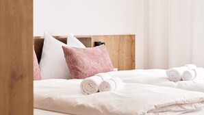 A neatly made bed with white linens and pink pillows, a wooden headboard, and rolled towels on the bed. - Alpenstolz #1.06 Comfort (Damüls)